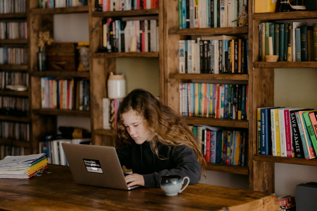 child working on a computer with lots of books behind her