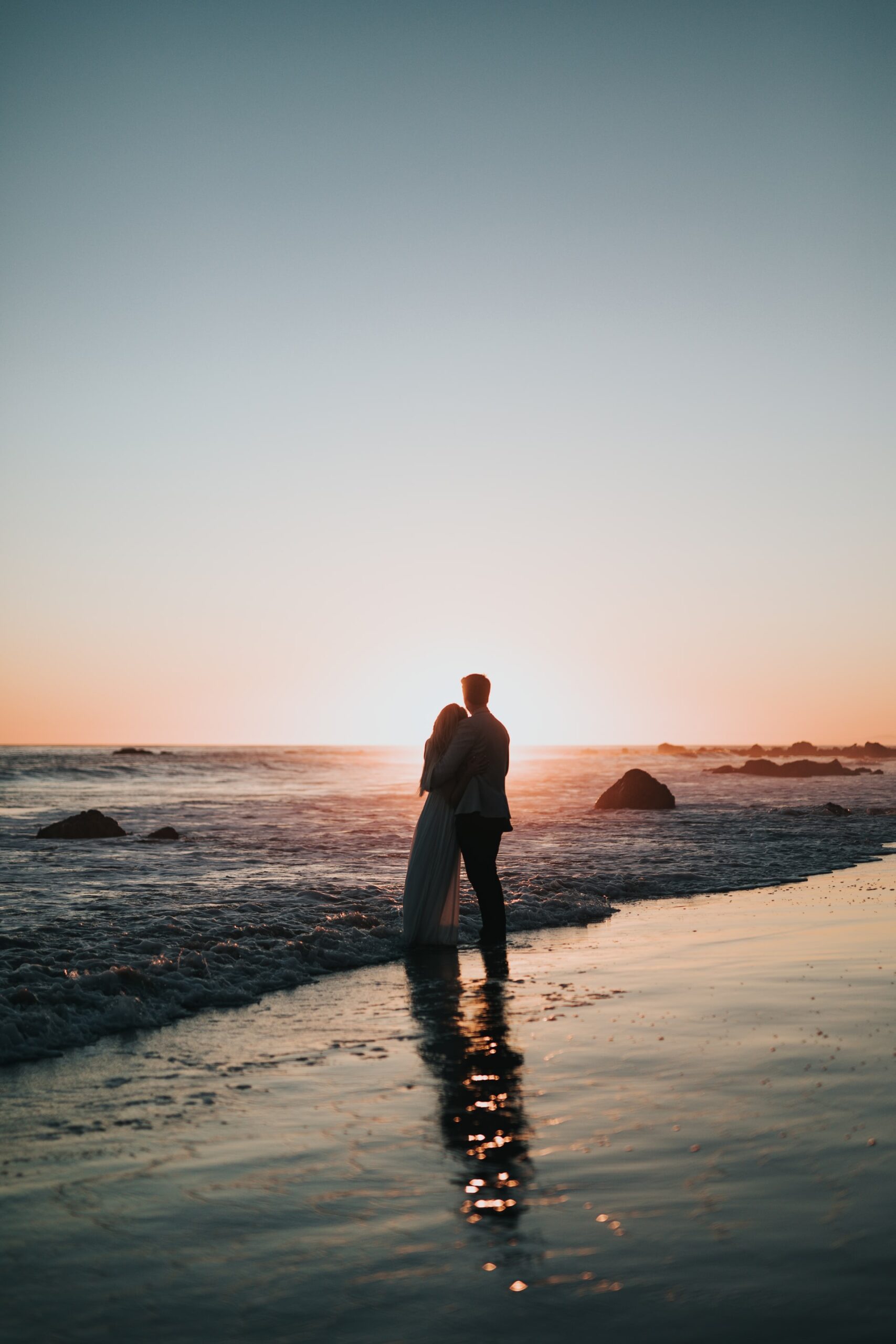 long distance wedding planning tips view of couple on a beach hugging at sunset