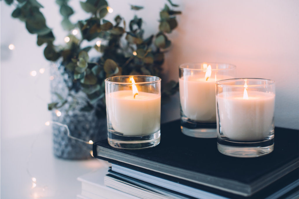 best candle scents for your living room. Pic of 3 lit candles on a pile of books next to a small potted plant.